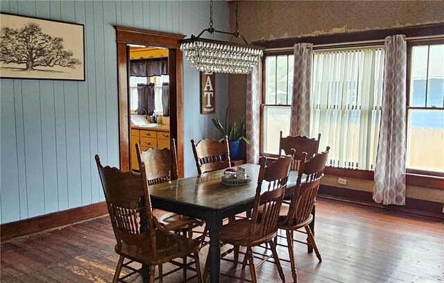 dining space featuring an inviting chandelier, wood walls, and dark hardwood / wood-style flooring