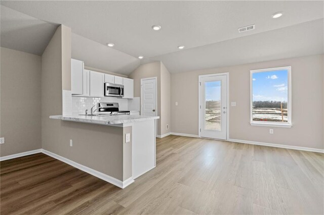 kitchen with tasteful backsplash, lofted ceiling, appliances with stainless steel finishes, white cabinets, and light wood-type flooring