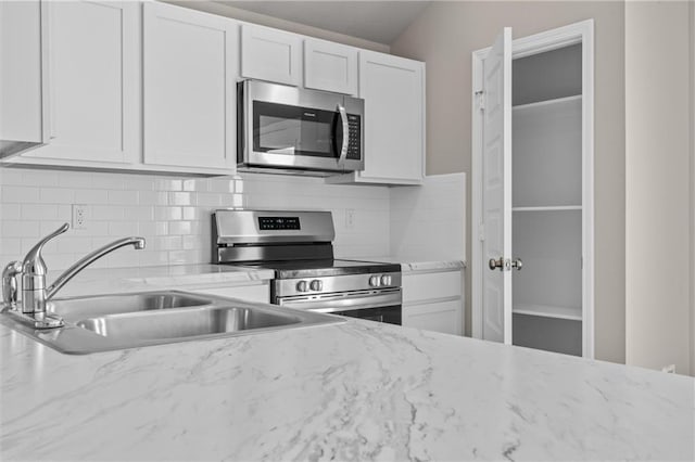 kitchen with light stone counters, stainless steel appliances, a sink, white cabinets, and tasteful backsplash