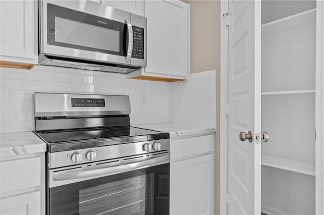 kitchen with appliances with stainless steel finishes, white cabinets, decorative backsplash, and light stone countertops