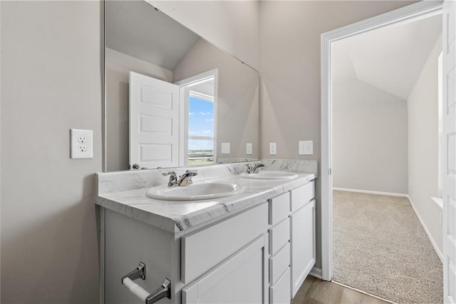 bathroom with lofted ceiling, double vanity, a sink, and baseboards