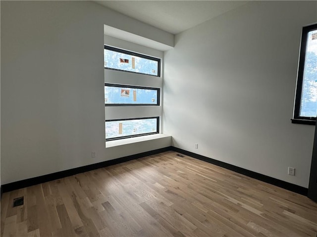 empty room featuring wood finished floors, visible vents, and baseboards