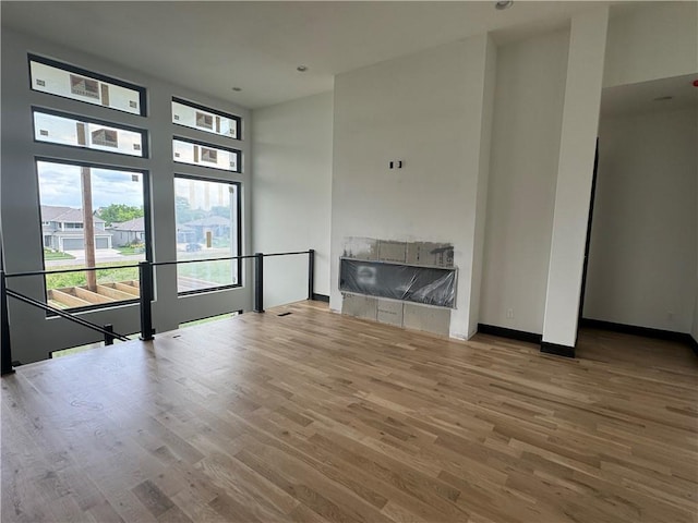 unfurnished living room with baseboards, a fireplace, a high ceiling, and wood finished floors