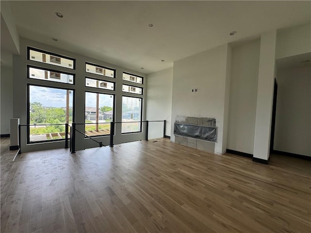 unfurnished living room with a towering ceiling, baseboards, wood finished floors, and recessed lighting