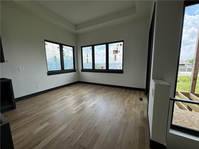 unfurnished room featuring a tray ceiling, light wood-type flooring, and baseboards