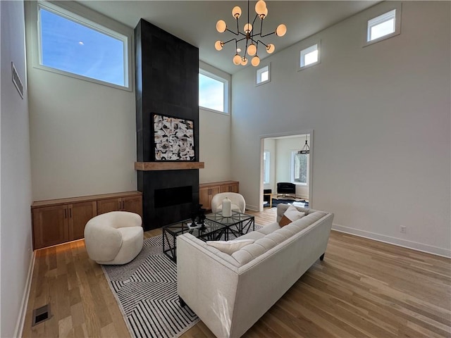 living room featuring a fireplace, light hardwood / wood-style flooring, a chandelier, and a high ceiling