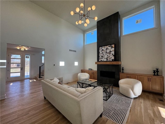 living room featuring an inviting chandelier, a towering ceiling, a fireplace, and hardwood / wood-style floors