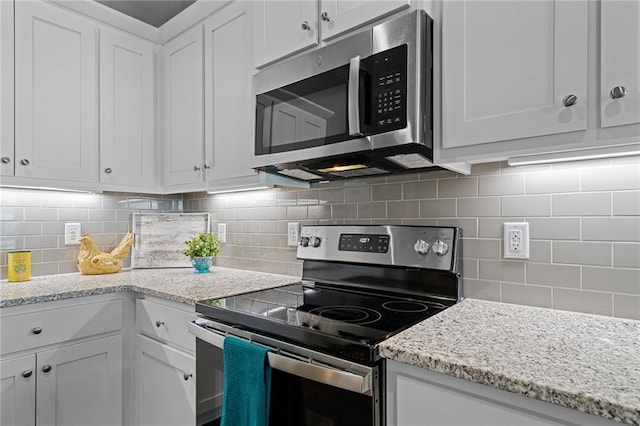 kitchen featuring appliances with stainless steel finishes, light stone countertops, white cabinets, and tasteful backsplash