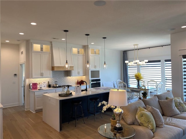 kitchen featuring a kitchen island with sink, decorative backsplash, oven, and white cabinets