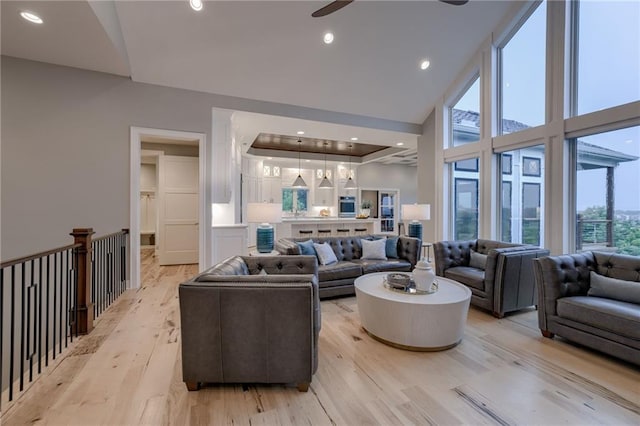 living room with light wood-type flooring, ceiling fan, a high ceiling, and a tray ceiling