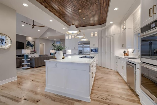 kitchen featuring an island with sink, built in appliances, sink, white cabinets, and pendant lighting