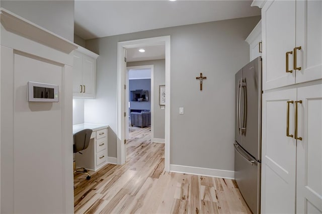 interior space with light hardwood / wood-style floors, white cabinetry, built in desk, and stainless steel refrigerator