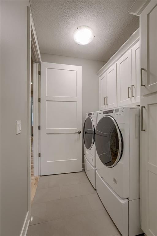 clothes washing area with washing machine and clothes dryer, cabinets, and a textured ceiling