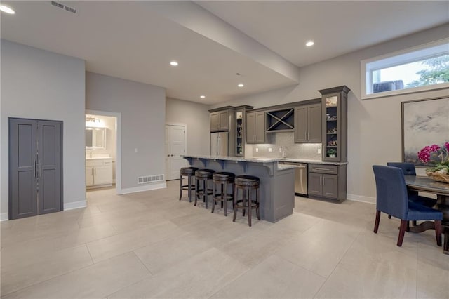 kitchen featuring tasteful backsplash, light stone counters, a center island, gray cabinets, and a kitchen bar