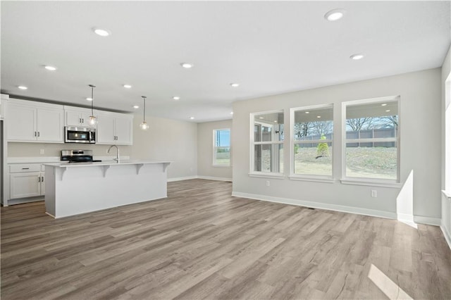 kitchen featuring a kitchen island with sink, light wood-type flooring, appliances with stainless steel finishes, decorative light fixtures, and white cabinetry