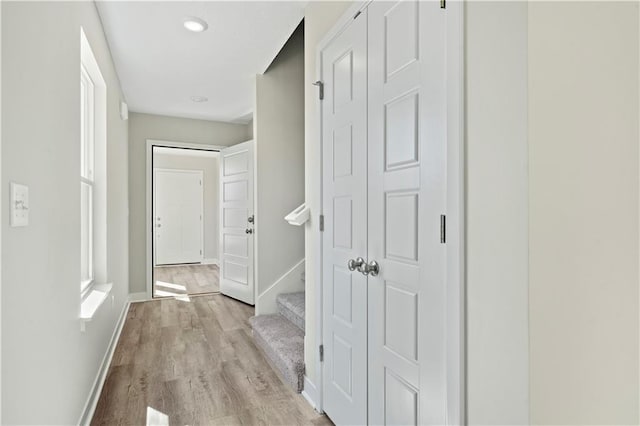 hallway with light wood-style floors, stairway, and baseboards