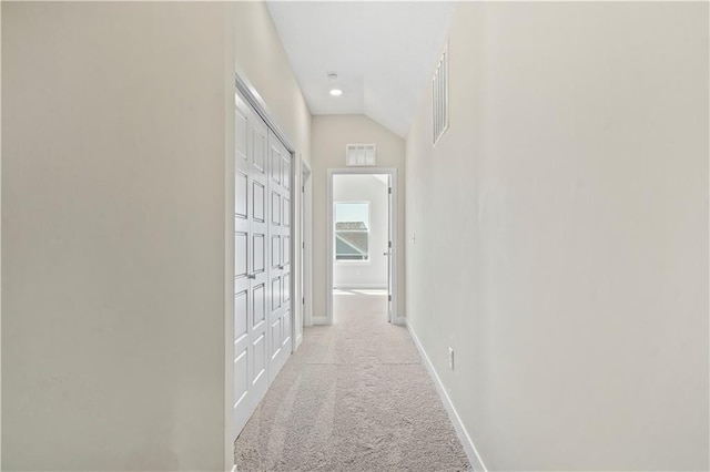 hall featuring baseboards, lofted ceiling, visible vents, and light colored carpet