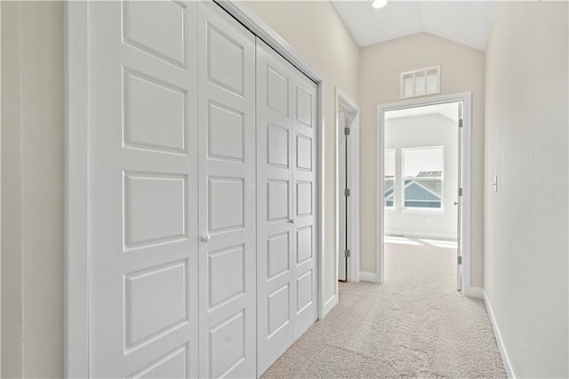 hallway featuring light colored carpet, vaulted ceiling, visible vents, and baseboards