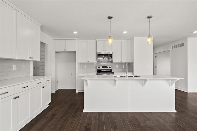 kitchen featuring appliances with stainless steel finishes, a center island with sink, decorative backsplash, and dark hardwood / wood-style floors