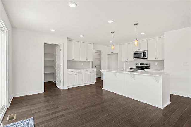 kitchen with dark hardwood / wood-style floors, an island with sink, white cabinets, decorative light fixtures, and stainless steel appliances