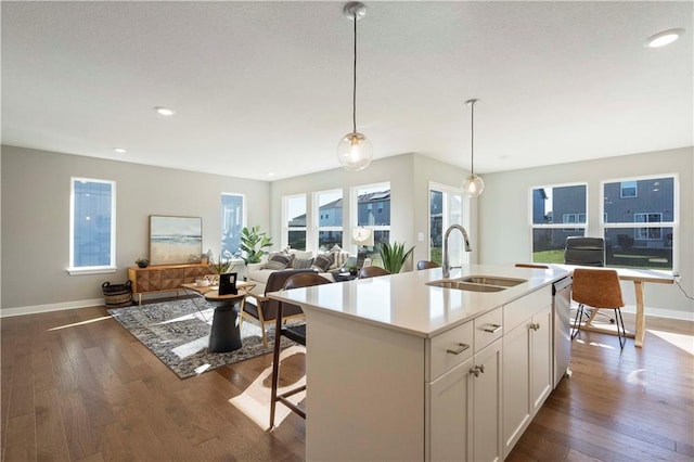 kitchen featuring decorative light fixtures, hardwood / wood-style floors, white cabinetry, sink, and an island with sink