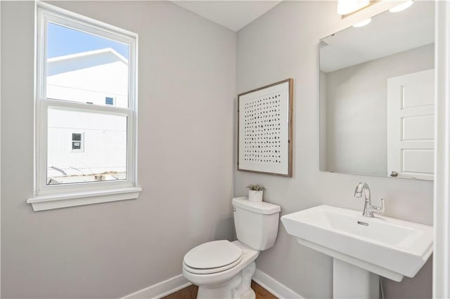 half bathroom featuring toilet, a sink, baseboards, and a wealth of natural light