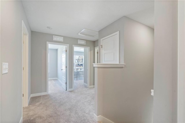 corridor with attic access, light colored carpet, and baseboards