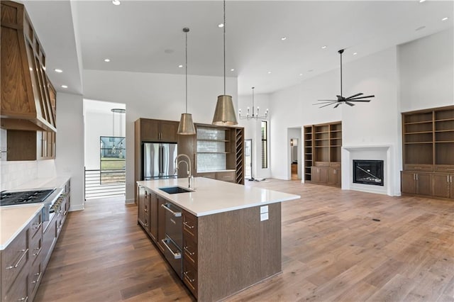 kitchen with wood-type flooring, an island with sink, appliances with stainless steel finishes, and high vaulted ceiling