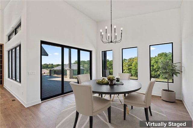 dining space featuring a high ceiling, light wood-type flooring, plenty of natural light, and an inviting chandelier