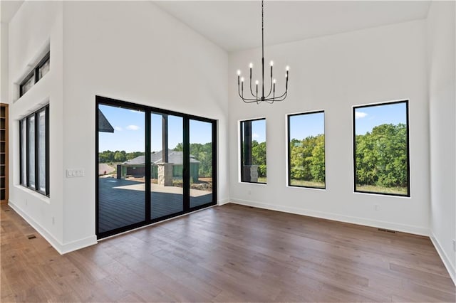 empty room featuring a high ceiling, hardwood / wood-style flooring, a wealth of natural light, and an inviting chandelier