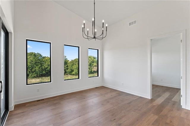 empty room with high vaulted ceiling, a chandelier, and light hardwood / wood-style floors