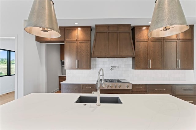 kitchen featuring custom range hood, light stone countertops, backsplash, and sink