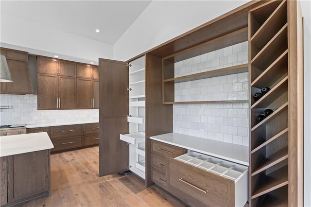 kitchen featuring tasteful backsplash, light hardwood / wood-style floors, wall chimney exhaust hood, and lofted ceiling