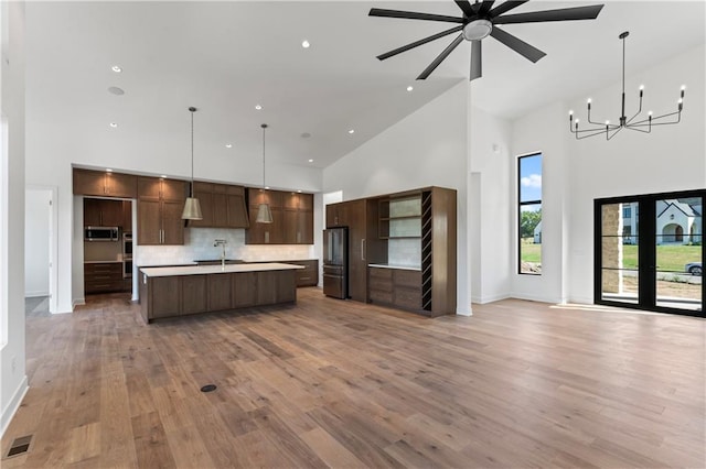 kitchen with a kitchen island with sink, pendant lighting, ceiling fan with notable chandelier, light hardwood / wood-style flooring, and high vaulted ceiling