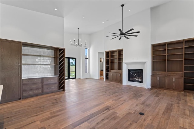 unfurnished living room with ceiling fan with notable chandelier, a towering ceiling, and hardwood / wood-style floors