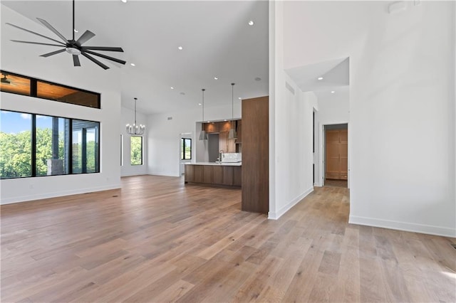 unfurnished living room featuring ceiling fan with notable chandelier, light wood-type flooring, and a high ceiling