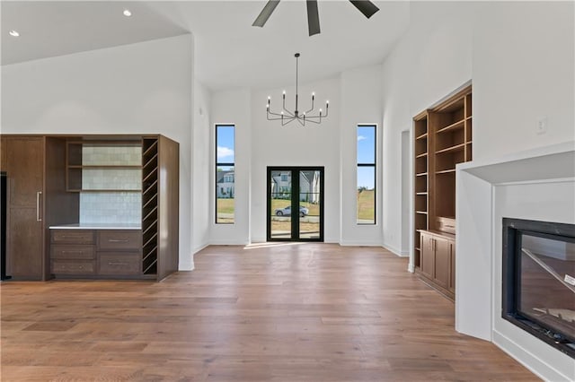 foyer entrance with ceiling fan with notable chandelier, high vaulted ceiling, and light hardwood / wood-style flooring