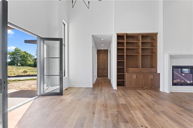 unfurnished living room with light wood-type flooring and a towering ceiling