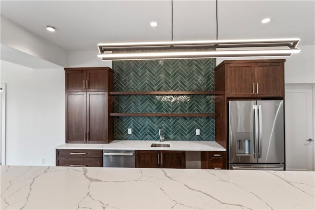 kitchen with tasteful backsplash, appliances with stainless steel finishes, light stone counters, and sink