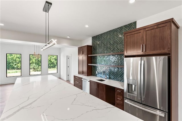 kitchen featuring hanging light fixtures, stainless steel refrigerator with ice dispenser, light stone counters, and sink