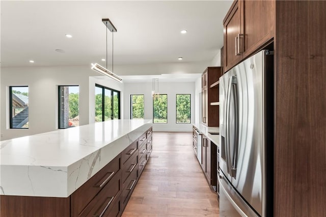 kitchen featuring light stone countertops, light hardwood / wood-style floors, hanging light fixtures, a large island, and stainless steel refrigerator with ice dispenser