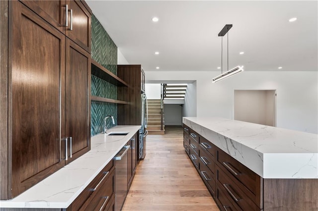 kitchen featuring light hardwood / wood-style floors, decorative light fixtures, light stone counters, sink, and dishwasher