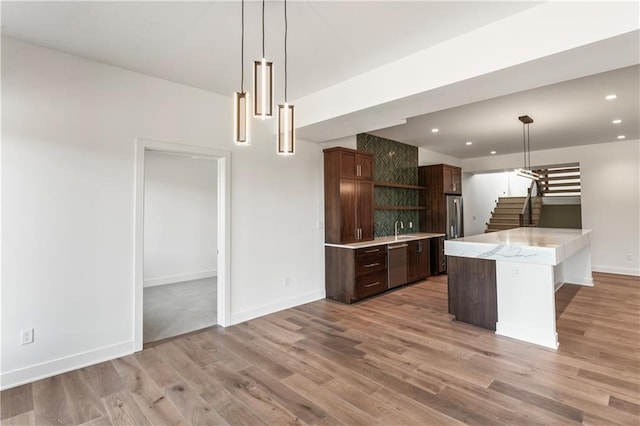 kitchen featuring stainless steel appliances, pendant lighting, light hardwood / wood-style floors, and dark brown cabinets