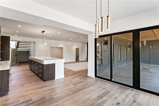 kitchen with hanging light fixtures, light hardwood / wood-style floors, a center island, and dark brown cabinets