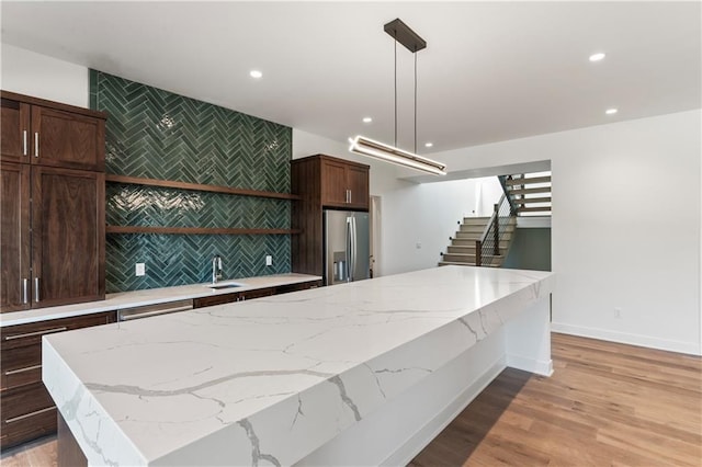 kitchen with pendant lighting, a kitchen island, light hardwood / wood-style flooring, light stone countertops, and stainless steel fridge with ice dispenser