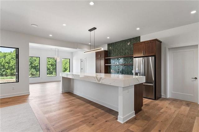 kitchen with a kitchen island, light stone countertops, pendant lighting, light hardwood / wood-style flooring, and stainless steel fridge with ice dispenser