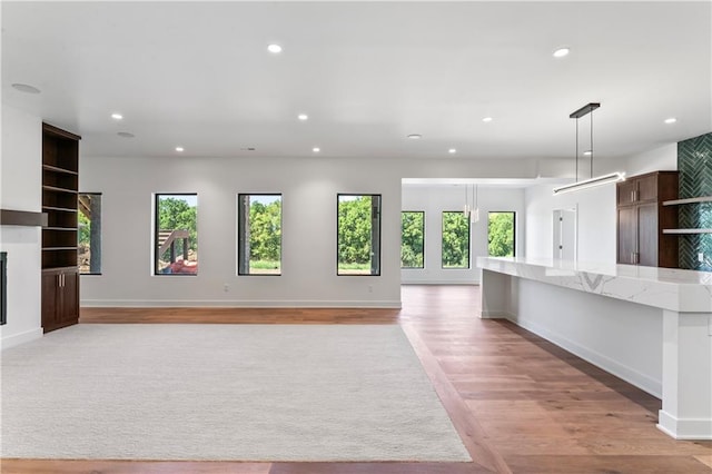 kitchen featuring light stone counters, pendant lighting, light hardwood / wood-style flooring, and a healthy amount of sunlight