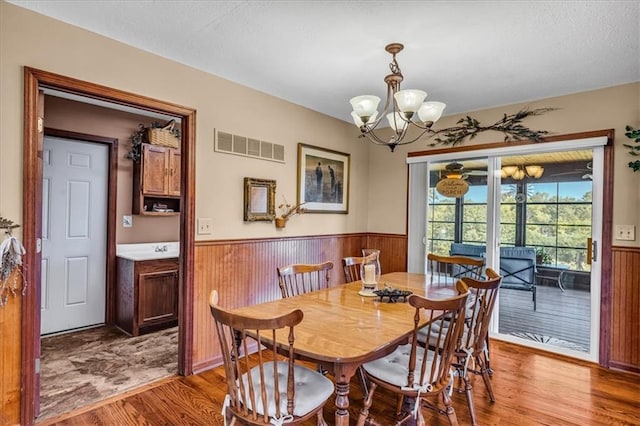 dining room with visible vents, a wainscoted wall, wood finished floors, wood walls, and a chandelier