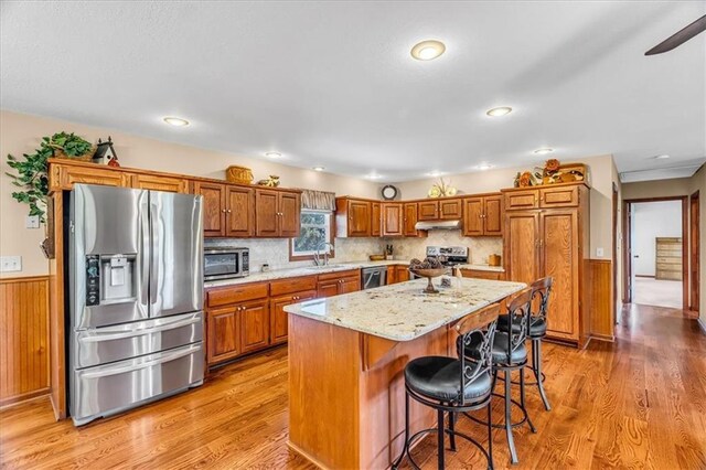 kitchen featuring light stone counters, a center island, sink, light hardwood / wood-style flooring, and appliances with stainless steel finishes