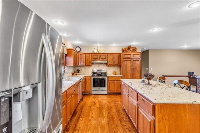 kitchen featuring tasteful backsplash, a kitchen island, stainless steel appliances, light hardwood / wood-style flooring, and sink